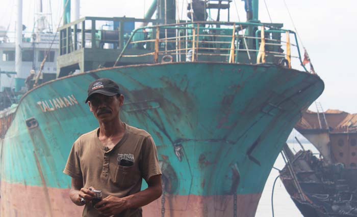 Takrip, mandor CV Sinar Agung Sejahtera berlatar belakang bangkai kapal yang siap dibantai, di Tanjung Jati, Kamal, Bangkalan. (foto: bahari)