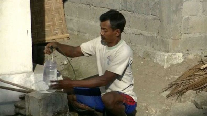 Seorang warga memanfaatkan toples untuk mengambil air bersih di bekas sumur bor. Untukmemenuhi 1 tangki butuh waktu 1 jam. (Foto: Antara)