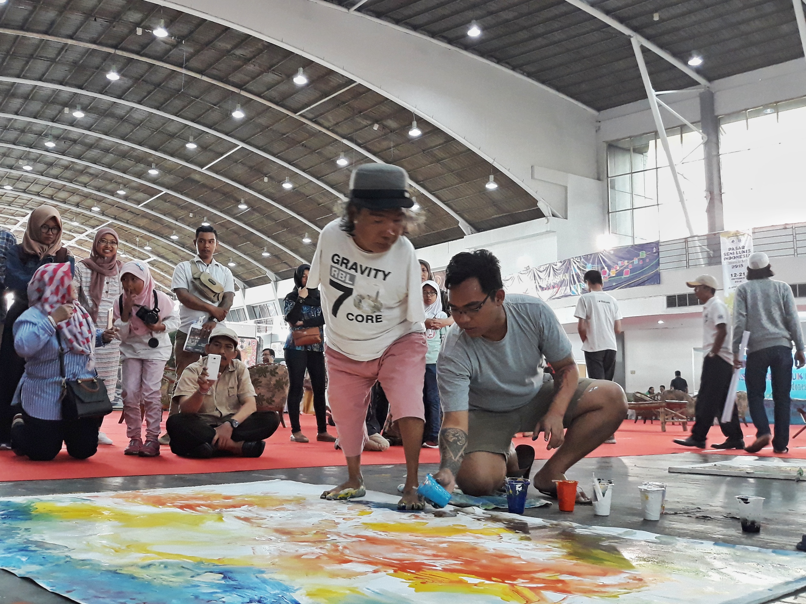 Sadikin Pard melukis di kanan panggung PSLI ke 11, dibantu Alrona Setiawan, putra sulungnya.