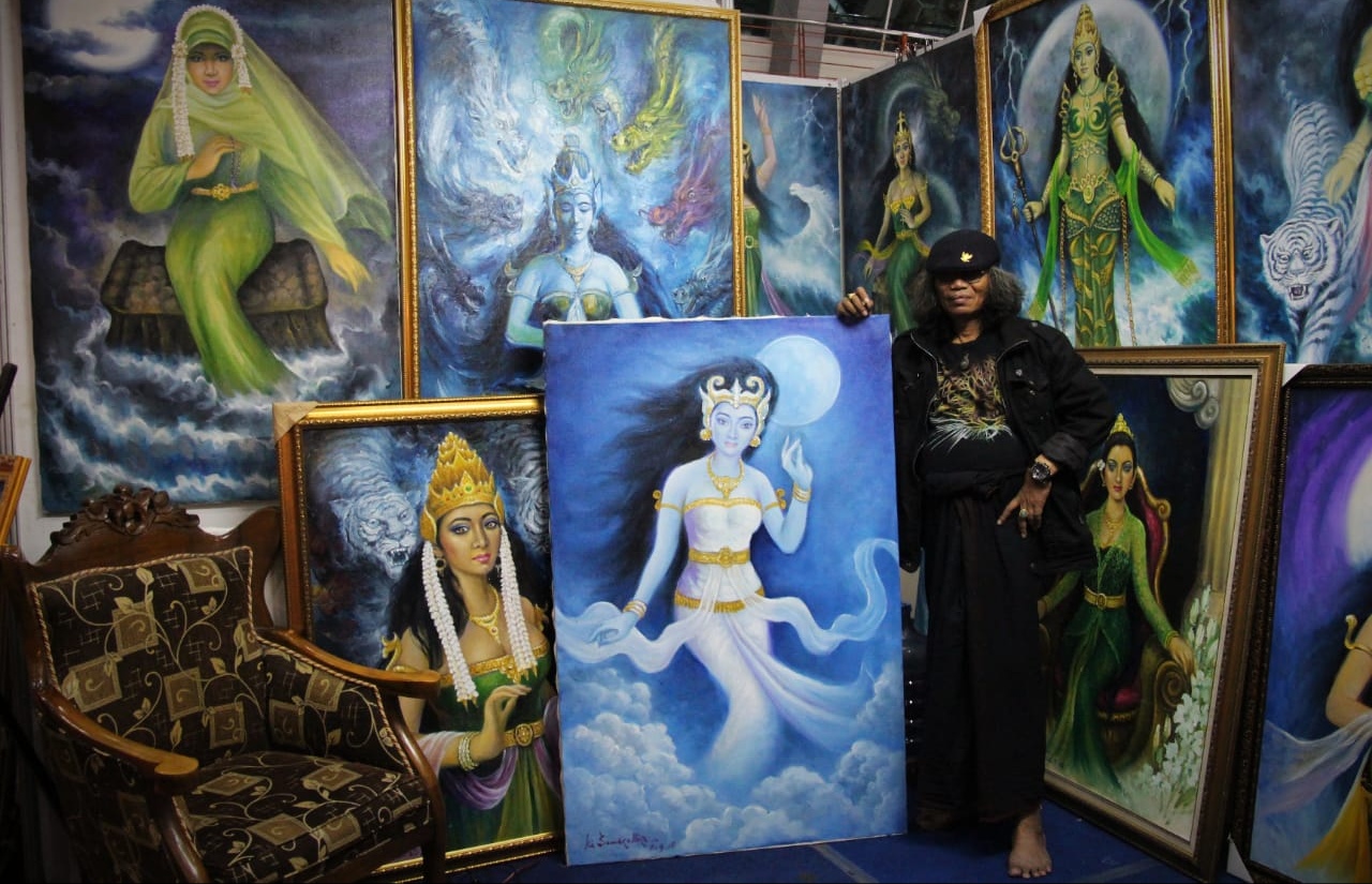 Ki Samudra Biru bersama lukisan-lukisan karyanya, di Pasar Seni Lukis Indonesia XI, di Surabaya. (Foto: ocan/ngopibareng.id) 