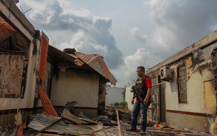 Seorang petugas gabungan berjaga di dekat puing bangunan rutan yang hangus terbakar pasca kerusuhan di Rutan Kelas II B Siak Sri Indrapura, Kabupaten Siak, Riau, Sabtu 11 Mei 2019. (Foto: Antara/Rony Muharrman)