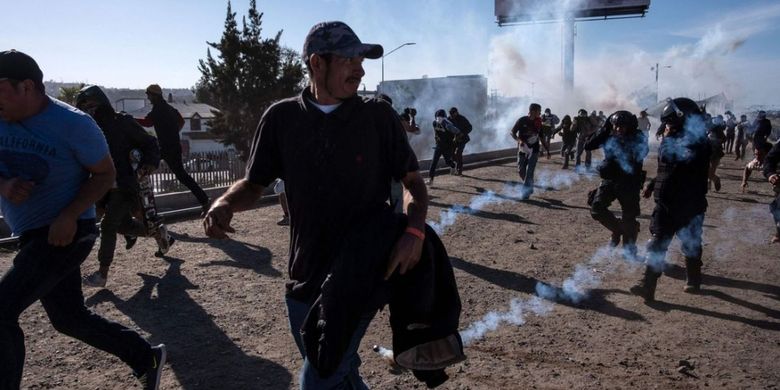 Para migran berlari menyelamatkan diri dari gas air mata yang ditembakkan polisi perbatasan Amerika Serikat-Meksiko Minggu 25 November 2018.(via Sky News)