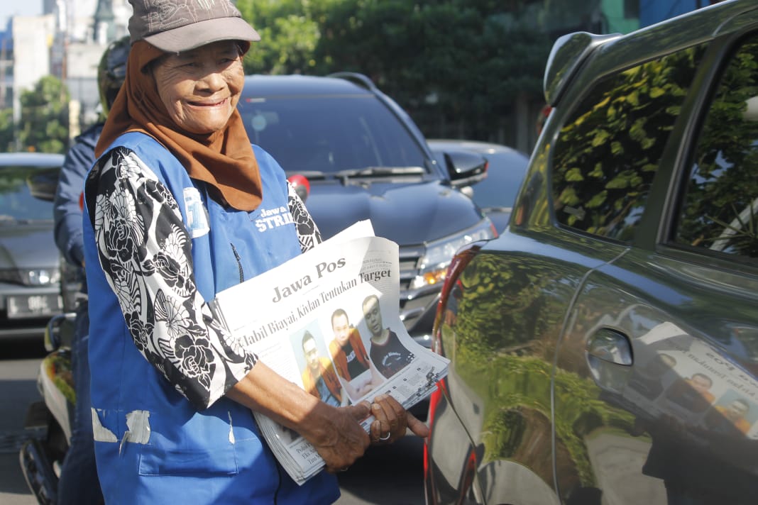 Mak Atik tetap jual koran di pinggir jalan meskipun  kejayaan penjual koran eceran sudah berlalu. (Foto: Asmanu/ngopibareng.id) 