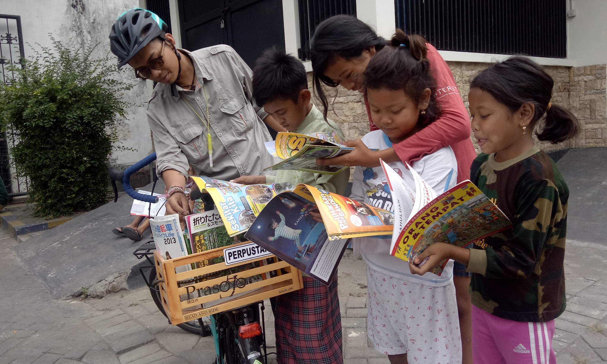 Yunaz Karaman bersama anak-anak dari kampung Srikana sedang membaca buku dari perputakaan keliling 'Prasojo'. (Foto: Pita/ngopibareng.id)