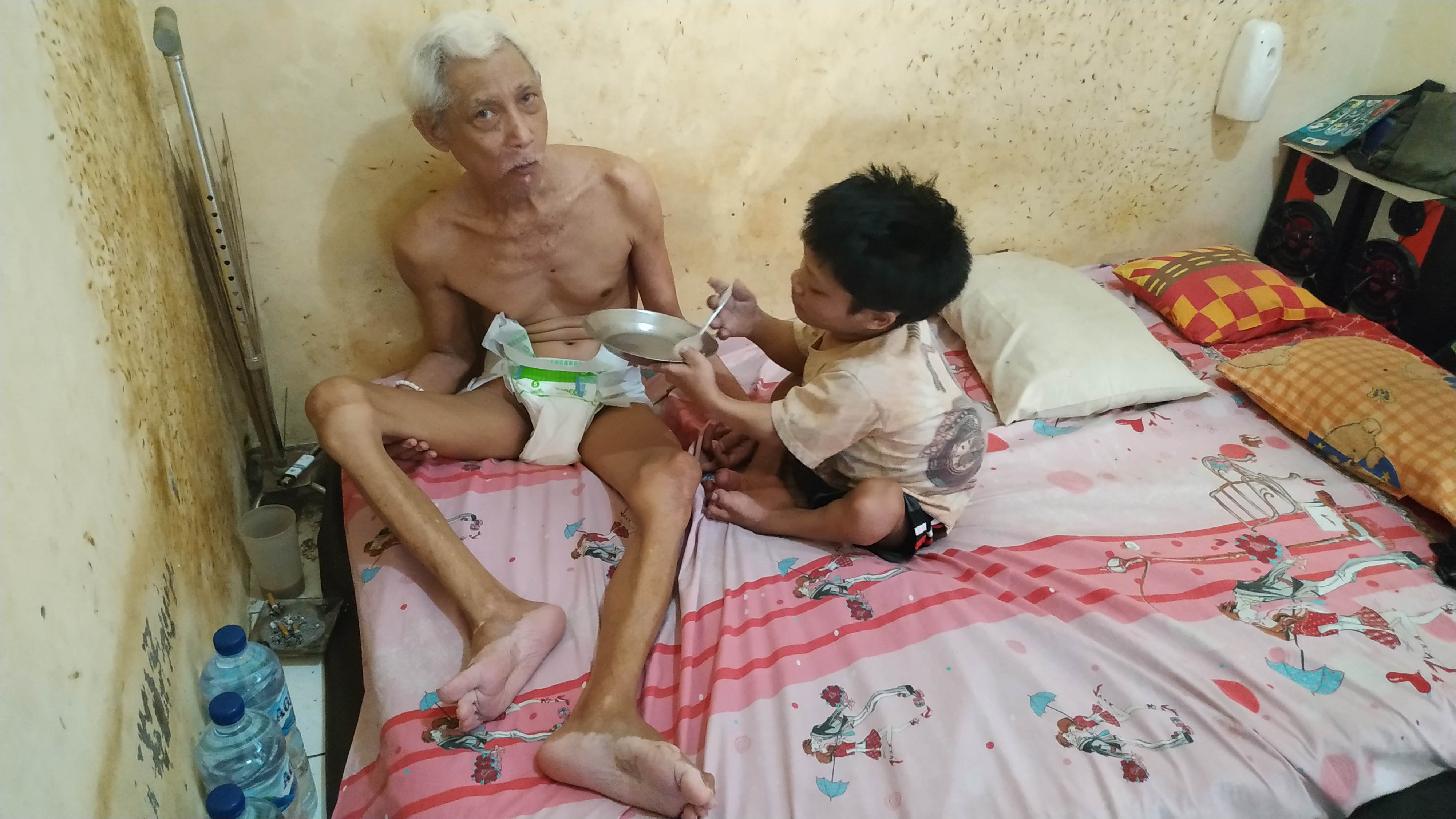 Erwin Kisyanto menyuapi orang tuanya yang menderita stroke. (Foto: Fendi/ngopibareng)