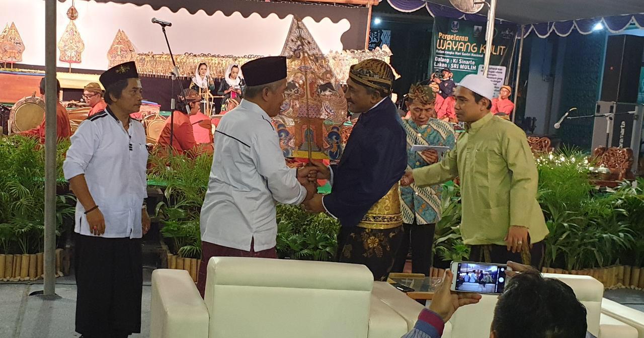 Ketua PWNU Jawa Timur KH Marzuki Mustamar menyerahkan Kayon kepada Ki Sinarto, sebelum pertunjukan Wayang Kulit. (Foto: riadi/ngopibareng.id)