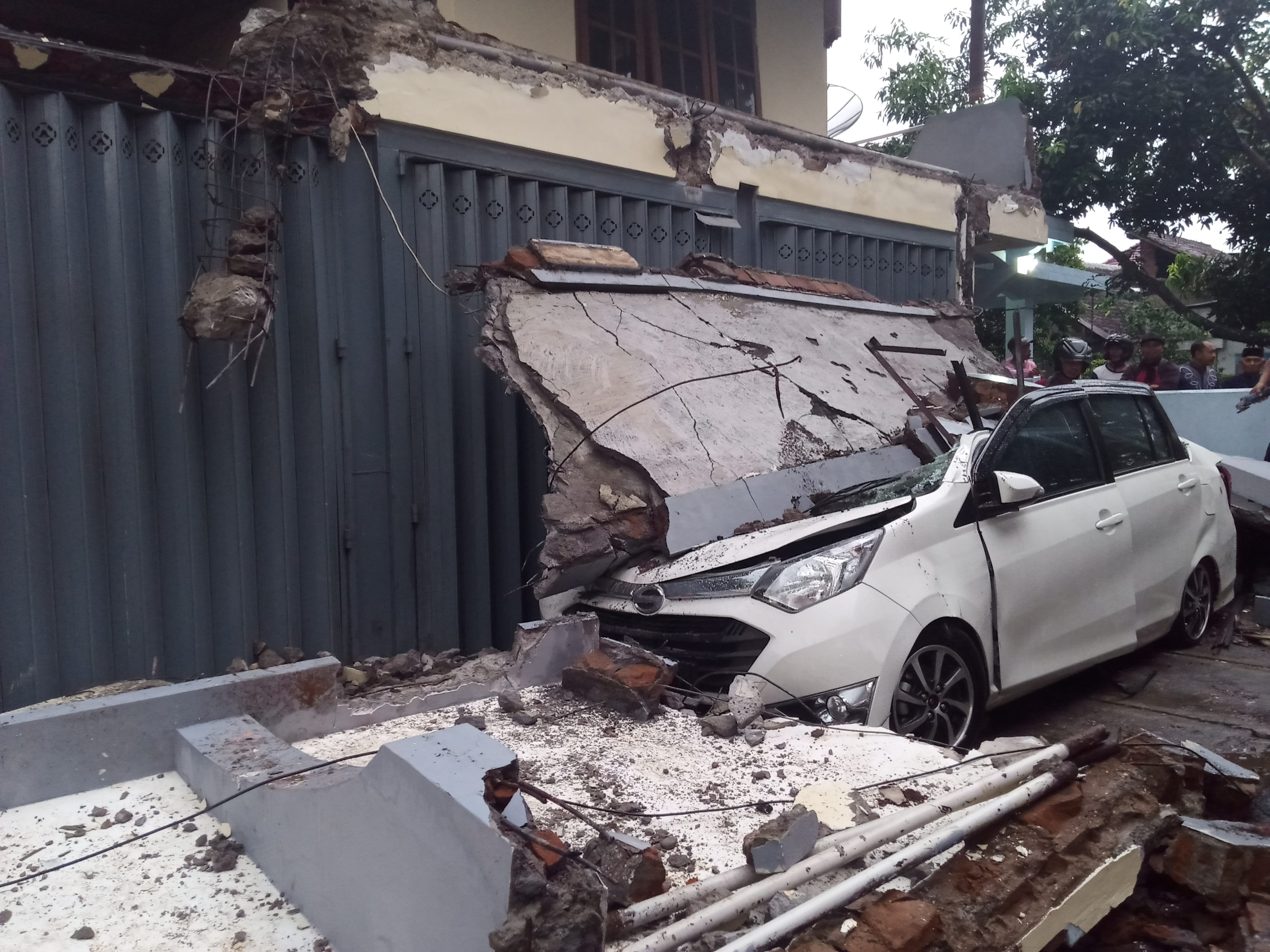 Satu unit mobil Daihatsu Sigra yang tertimpa runtuhan tembok ruko lantai 2 (Theo/ngopibareng.id)