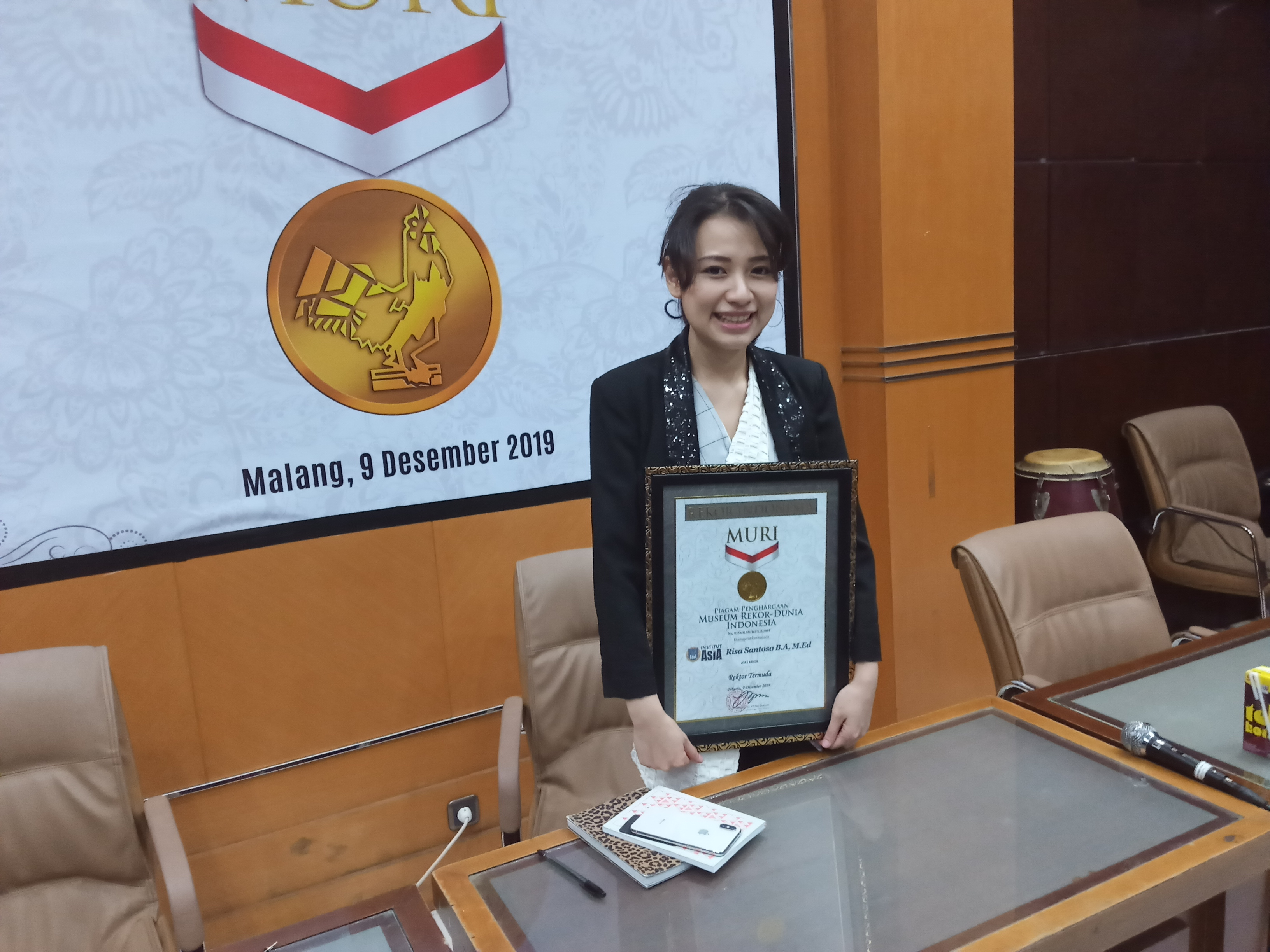 Rektor Termuda dari Institut Teknologi dan Bisnis (ITB) Asia, Risa Santoso saat memegang piagam penghargaan dari Museum Rekor Indonesia (Theo/ngopibareng.id)