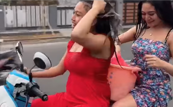 Tangakapan layar dua perempuan mandi di atas motor di jalan raya.