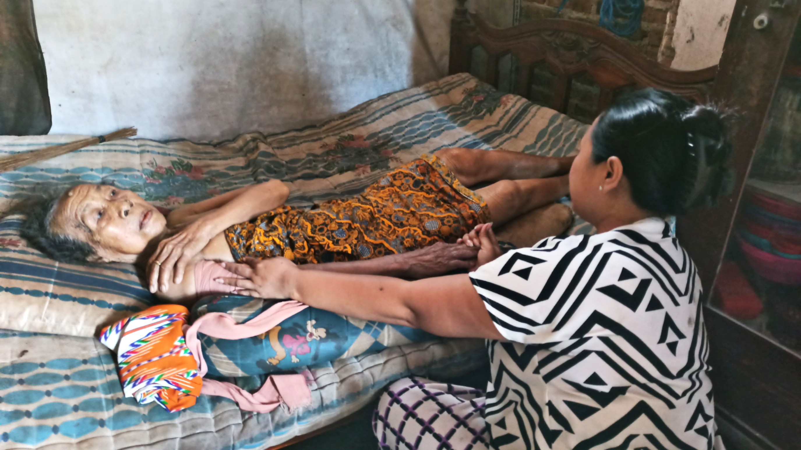 Nenek Nihayah terbaring sambil memegangi pangkal lengannya yang mengalami pergeseran sendi (foto : Hujaini/ngopibareng.id)