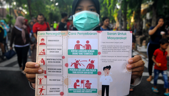 Seorang warga memperlihatkan leaflet seputar virus corona (Foto: Erfan Hazransyah/nopibareng.id)