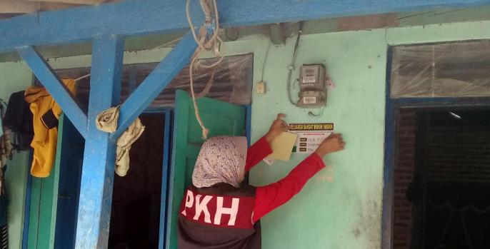 Seorang pendamping PKH menempel stiker di rumah keluarga penerima manfaat (KPM). Tahun ini KPM di Pasuruan turun. (Foto: Dok Humas)