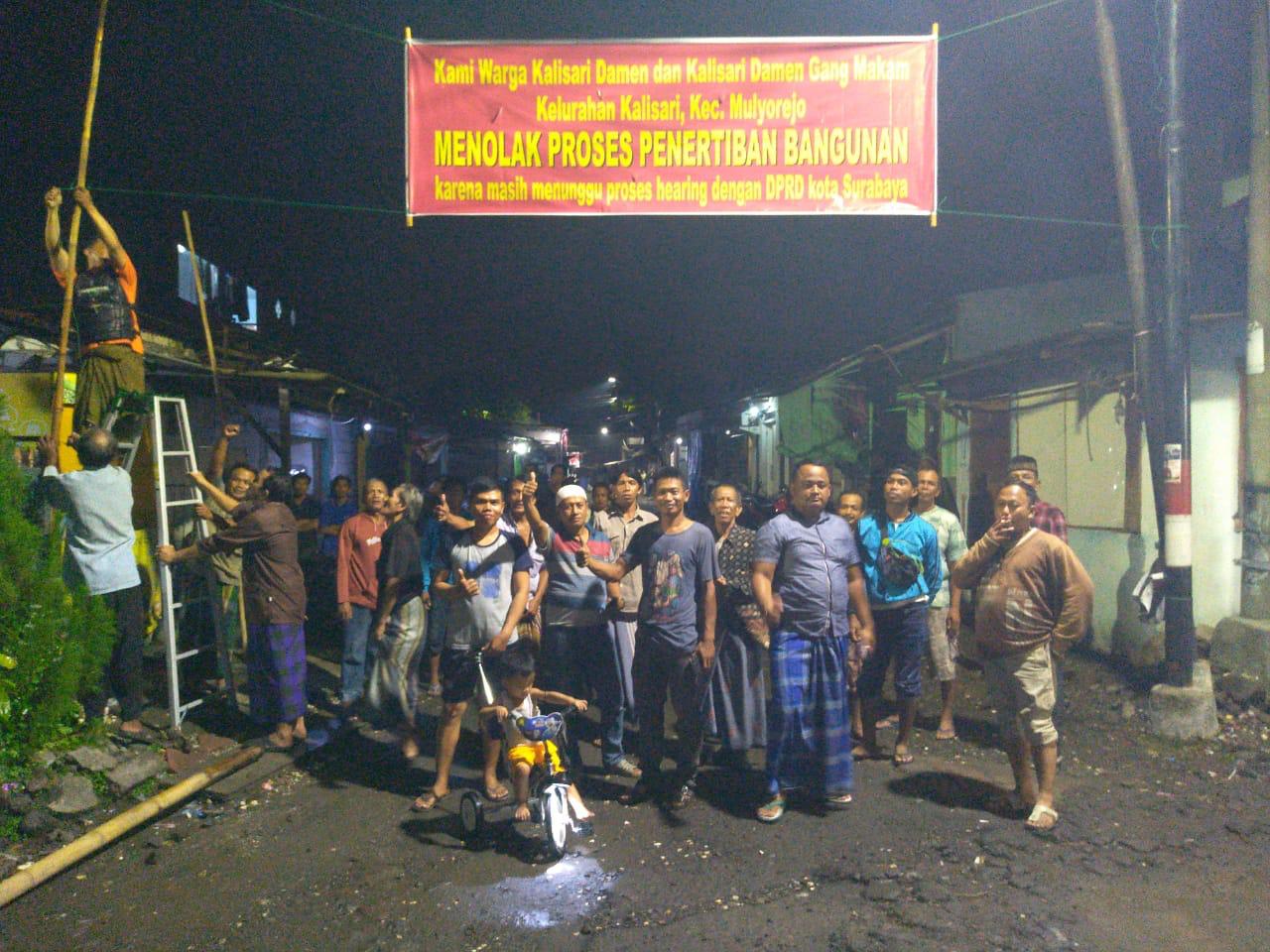 Warga Kalisari Damen Gang Makam saat memasang baliho penolakan penggusuran. (Foto: Ni'am Kurniawan/Ngopibareng.id)