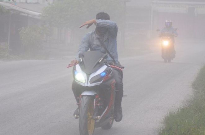 Seorang pengendara sepeda motor menutup mata karena terkena hujan abu dari erupsi Gunung Merapi. (Foto: Antara)