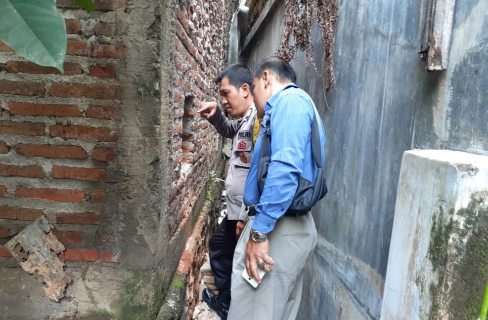 Petugas Polsek Srono mengecek lubang di tembok yang diduga tempat pelaku masuk ke dalam kantor Bank Jatim. (Foto: Istimewa)