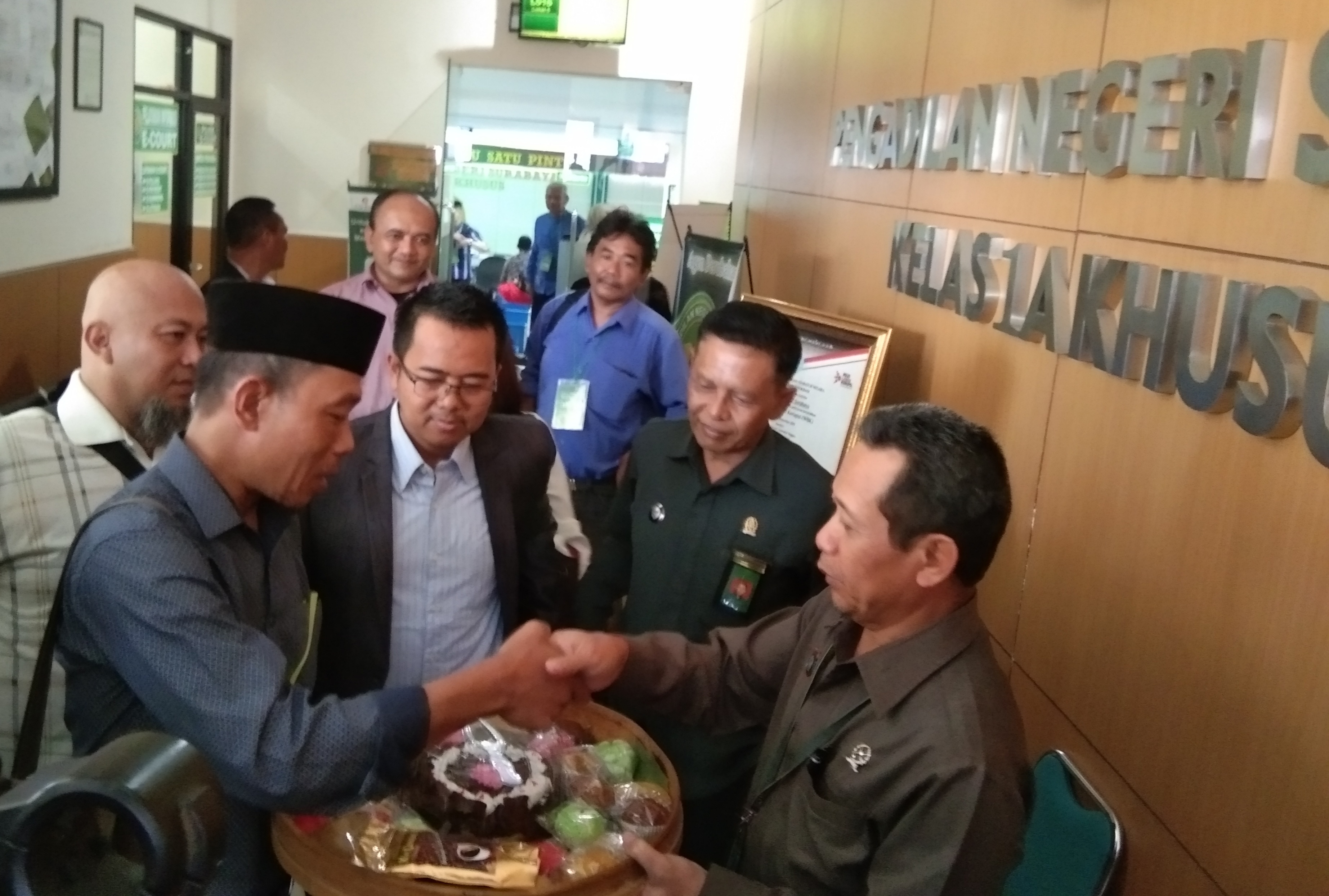 Kusnan Hadi (kiri) saat menyerahkan tumpeng kepada Ketua Pengadilan Negeri Surabaya, Nursyam (kanan) di PN Surabaya, Selasa, 10 Maret 2020. (Foto: Ni'am Kurniawan/Ngopibareng.id)