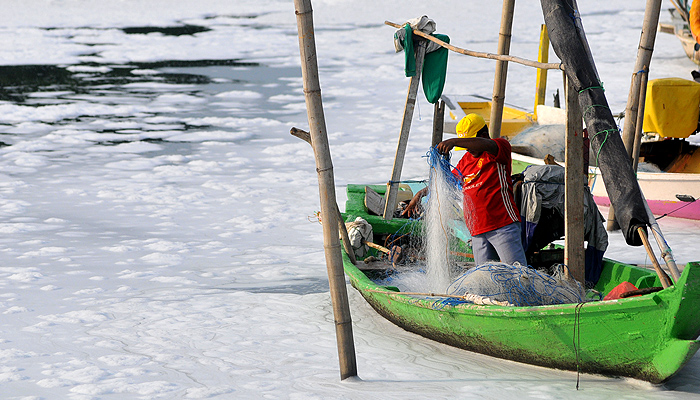 Nelayan beraktivitas di perahu saat bersandar di sekitar muara sungai Tambak Wedi, Surabaya, yang dipenuhi limbah busa putih. (Foto: Erfan Hazransyah/Ngopibareng.id)