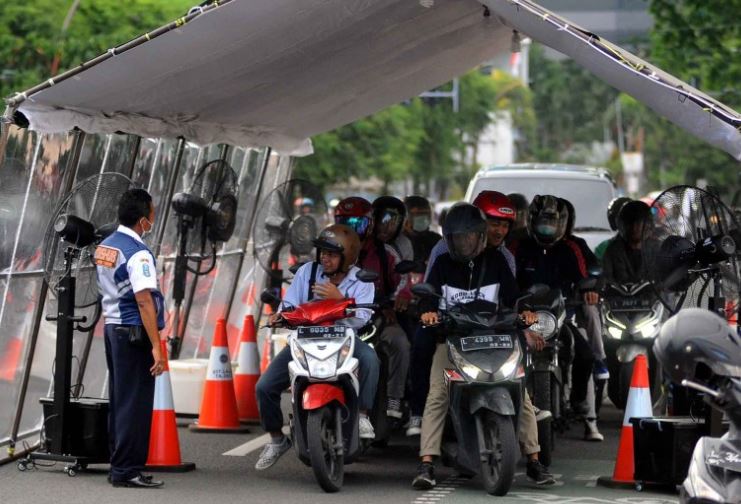 Petugas Dinas Perhubungan (Dishub) Jawa Timur memberi aba-aba agar kendaraan yang melintas di dalam bilik penyemprotan disinfektan untuk menghentikan kendaraannya sebentar. (Foto: Erfan Hazransyah/Ngopibareng.id)
