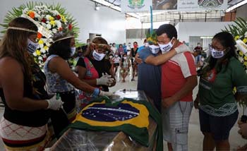 Miqueias Moreira Kokama (berkaos biru) memeluk kerabat saat mengikuti proses pemakaman ayahnya yang Kepala Suku Kokama, Messias Kokama, 53 tahun, yang  meninggal karena penyakit virus corona di Parque das Tribos, Amazon, Manaus, Brazil. (Foto:Antara/Reuters)