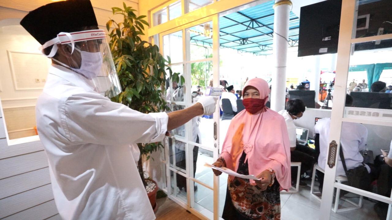 Warga diperiksa suhu tubuhnya sebelum masuk ke ruang pelayanan Desa Genteng Wetan. Petugas juga mengenakan masker dan alat pelindung wajah (Foto: istimewa)