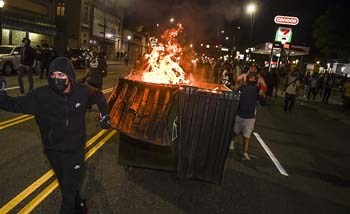 Para pengunjuk rasa membakar tempat sampah dan mendorongnya ke arah  barisan polisi di Denver, Colorado, Minggu malam. (Foto:Aljazeera/AFP)
