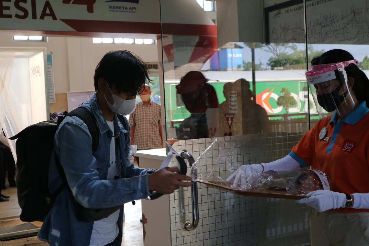 Salah satu penumpang kereta api di Stasiun Malang Kota Baru saat mengambil face shiel atau pelindung wajah yang disediakan PT. KAI. (Foto: Lalu Theo/Ngopibareng.id)