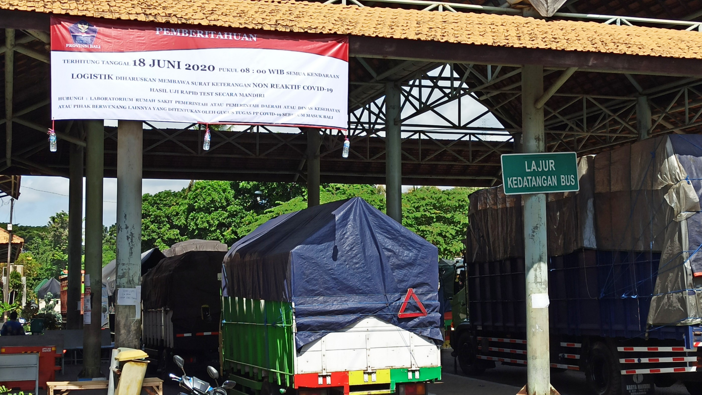 Antrean truk pengangkut logistik di check point terminal Sritanjung Banyuwangi. Pada bagian atas tampak spanduk tentang penghentian rapid test gratis untuk sopir kendaraan logistik (foto:Hujaini/Ngopibareng.id)
