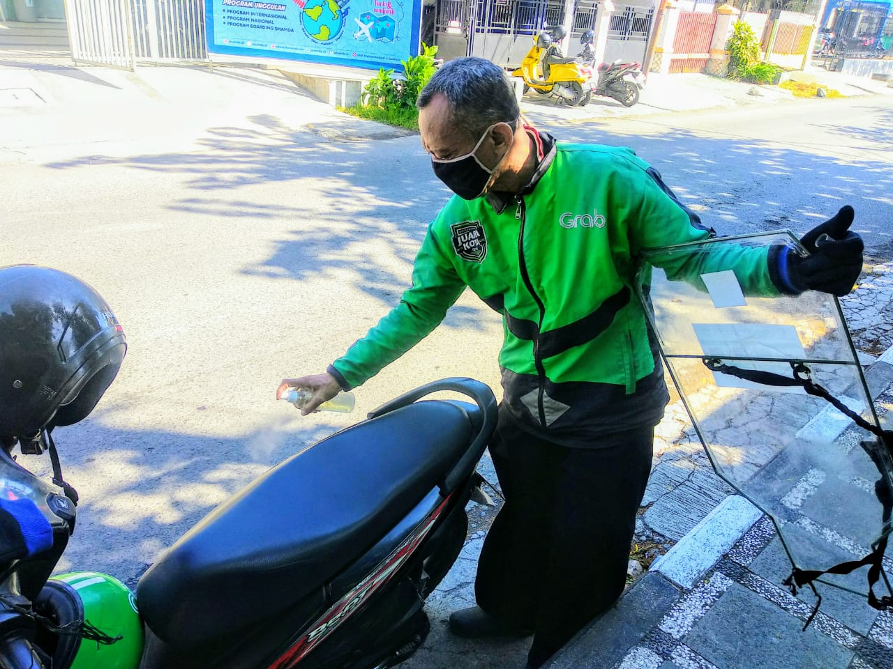 Nahrowi saat menyemprot disinfektan ke sepeda motornya sebelum mengantar penumpang (Foto: M.Rizqi/Ngopibareng.id)