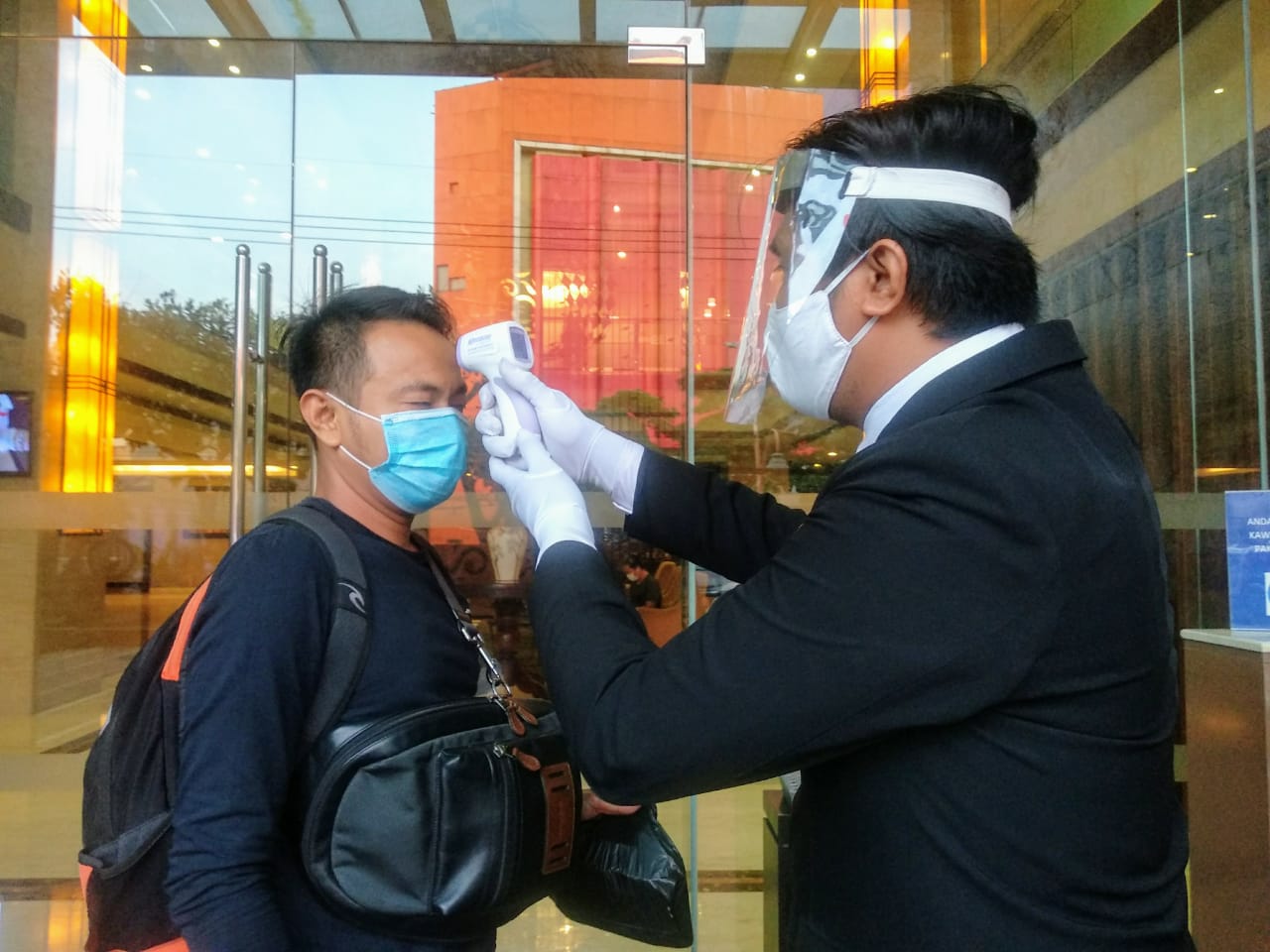 Petugas di depan hotel cek suhu badan pengunjung. (Foto: M.Rizqi/Ngopibareng.id)