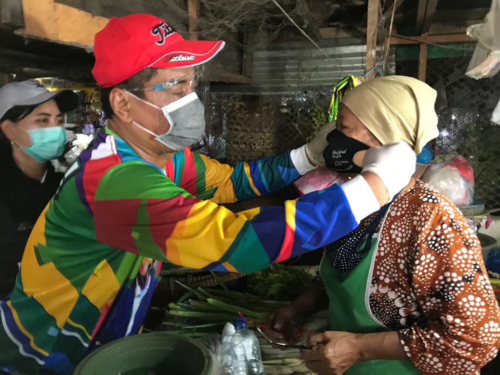 Bacawali Surabaya, Mujiaman Sukirno ketika memakaikan masker pada pedagang di Pasar Krukah, Surabaya. (Foto: Fariz Yarbo/Ngopibareng.id)