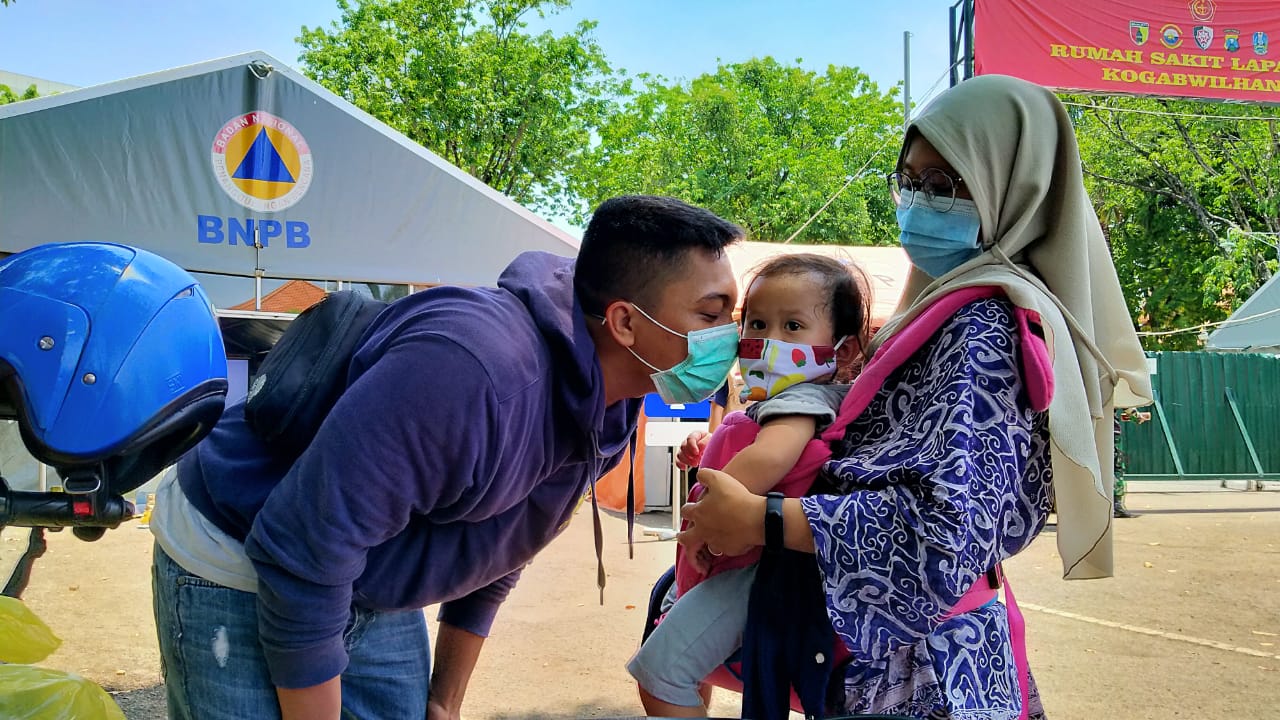 Erlangga Raditya (kiri) mencium anaknya, Ilana Tatiana Raditya (tengah) usai dinyatakan sembuh dari Covid-19 di RS Lapangan Kogabwilhan II Indrapura, Surabaya, Minggu 8 November 2020. (Foto: Fariz Yarbo/Ngopibareng.id)