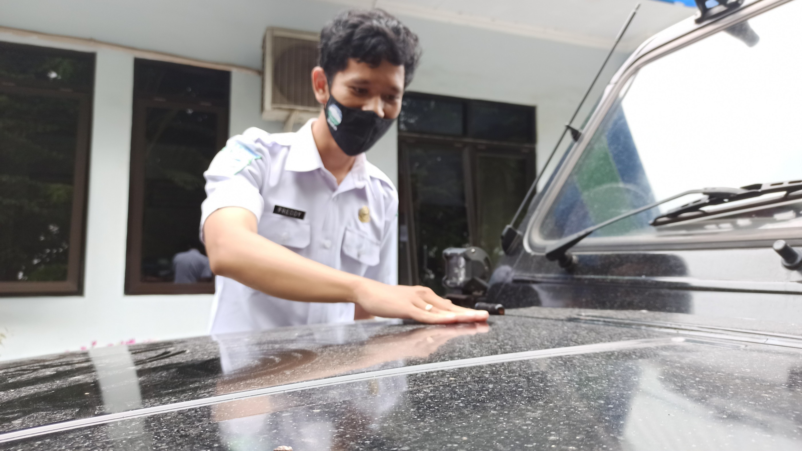 Prakirawan BMKG Stasiun Meteorologi Kelas III Banyuwangi, Freddy Dwi Kurniawan mengecek debu pada kap mobil yang ada di depan area parkir. (Foto: Muh Hujaini/Ngopibareng.id)