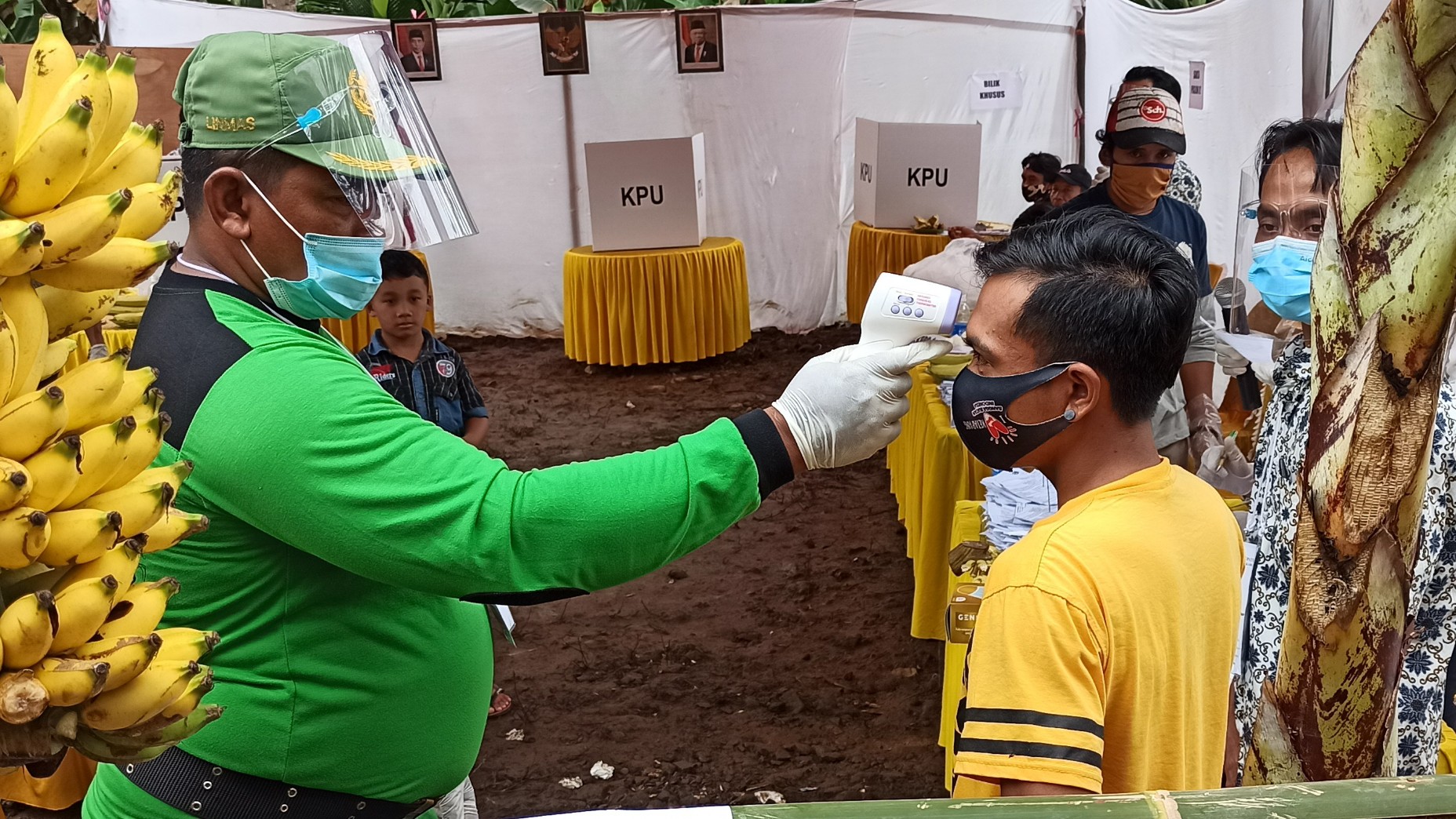 Petugas Kelompok Penyelenggara Pemungutan Suara (KPPS) sedang mengecek suhu tubuh salah satu pemilih, sebelum menyalurkan hak suaranya dibilik. (Foto: Muh Hujaini/Ngopibareng.id)