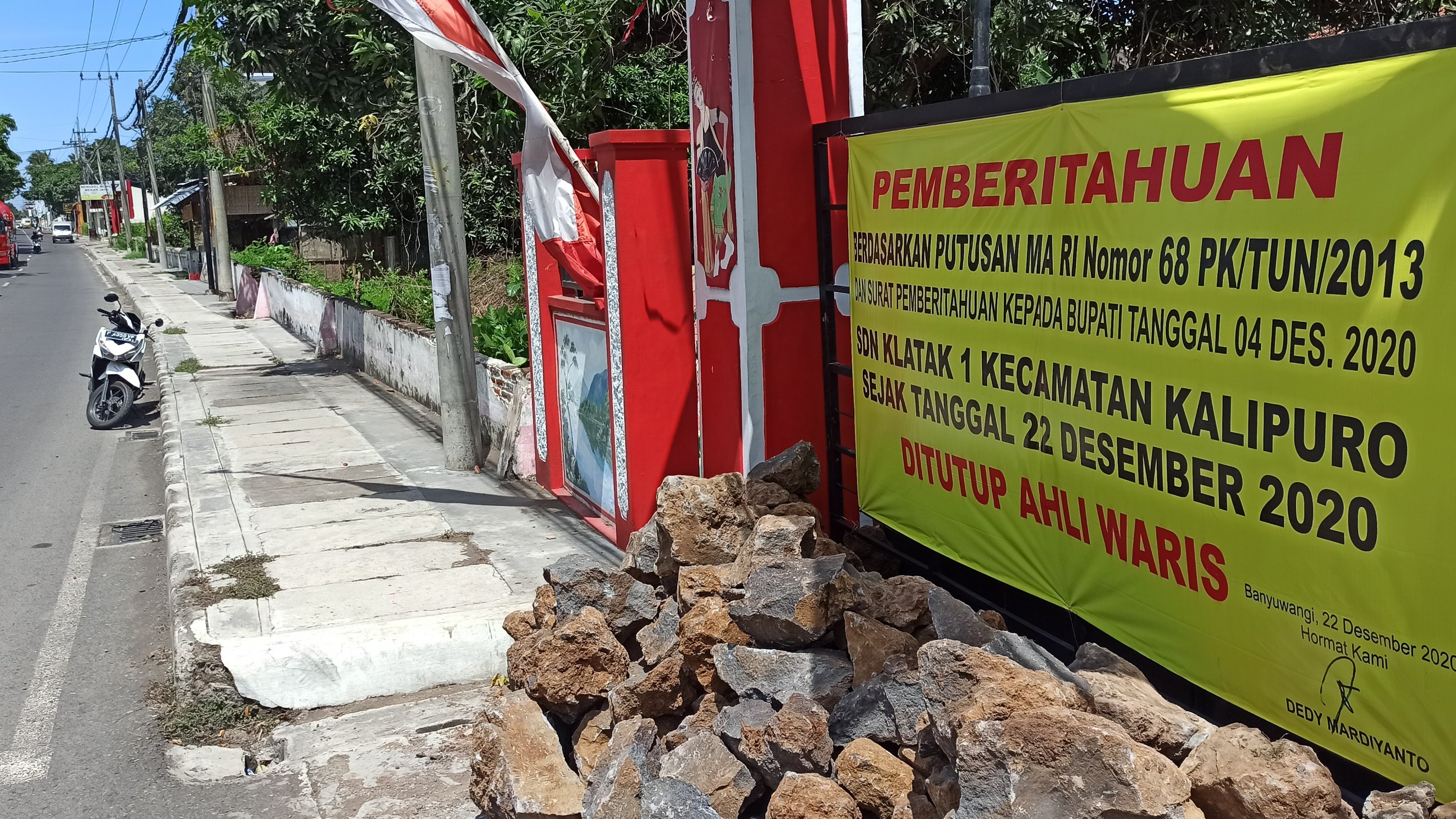 Banner penutupan dan batu yang dipasang di depan pintu masuk SDN 1 Klatak, Kecamatan Kalipuro Banyuwangi (foto: Muh Hujaini/Ngopibareng.id)