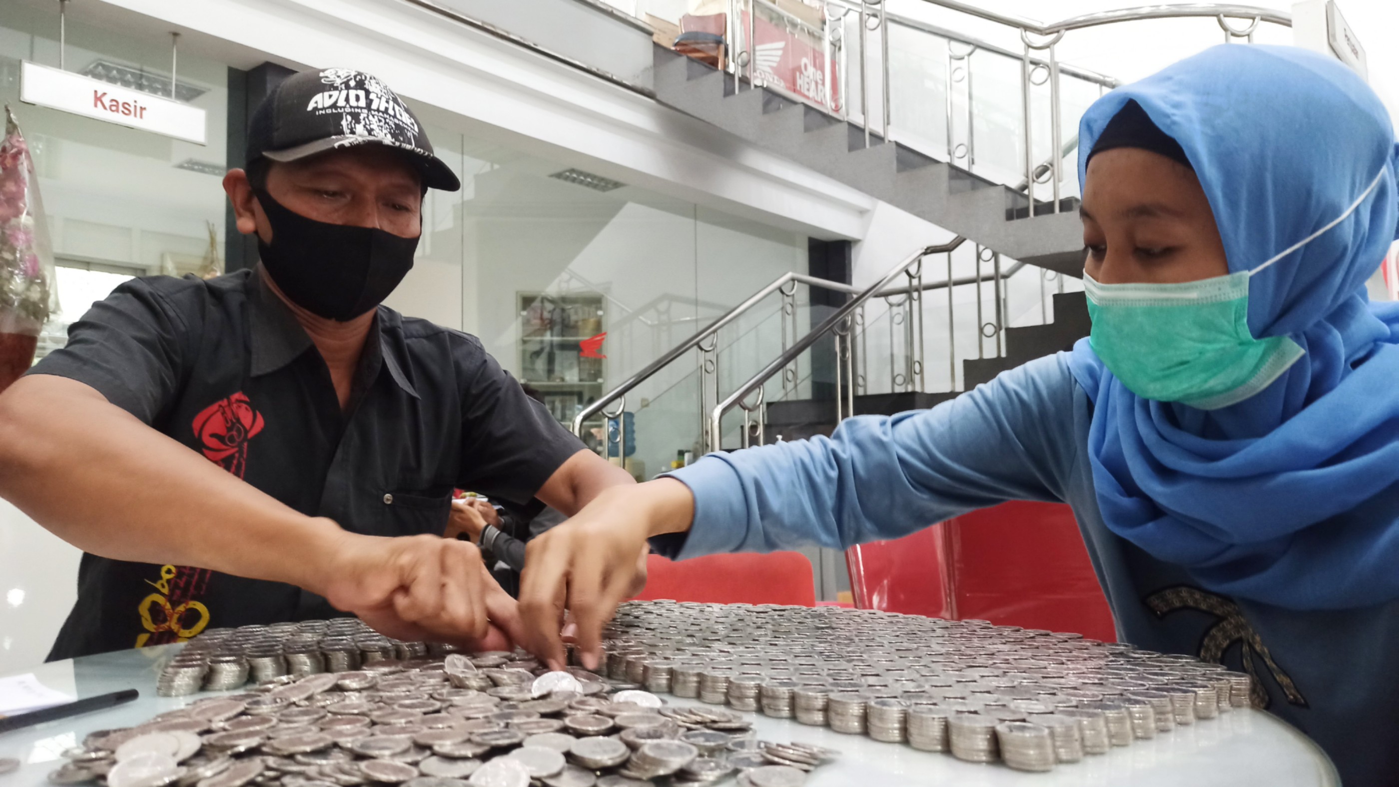Amidah (kanan) dibantu konsumen lain sedang menghitung uang koin untuk mbeli sepeda motor baru (foto:Muh Hujaini/Ngopibareng.id)