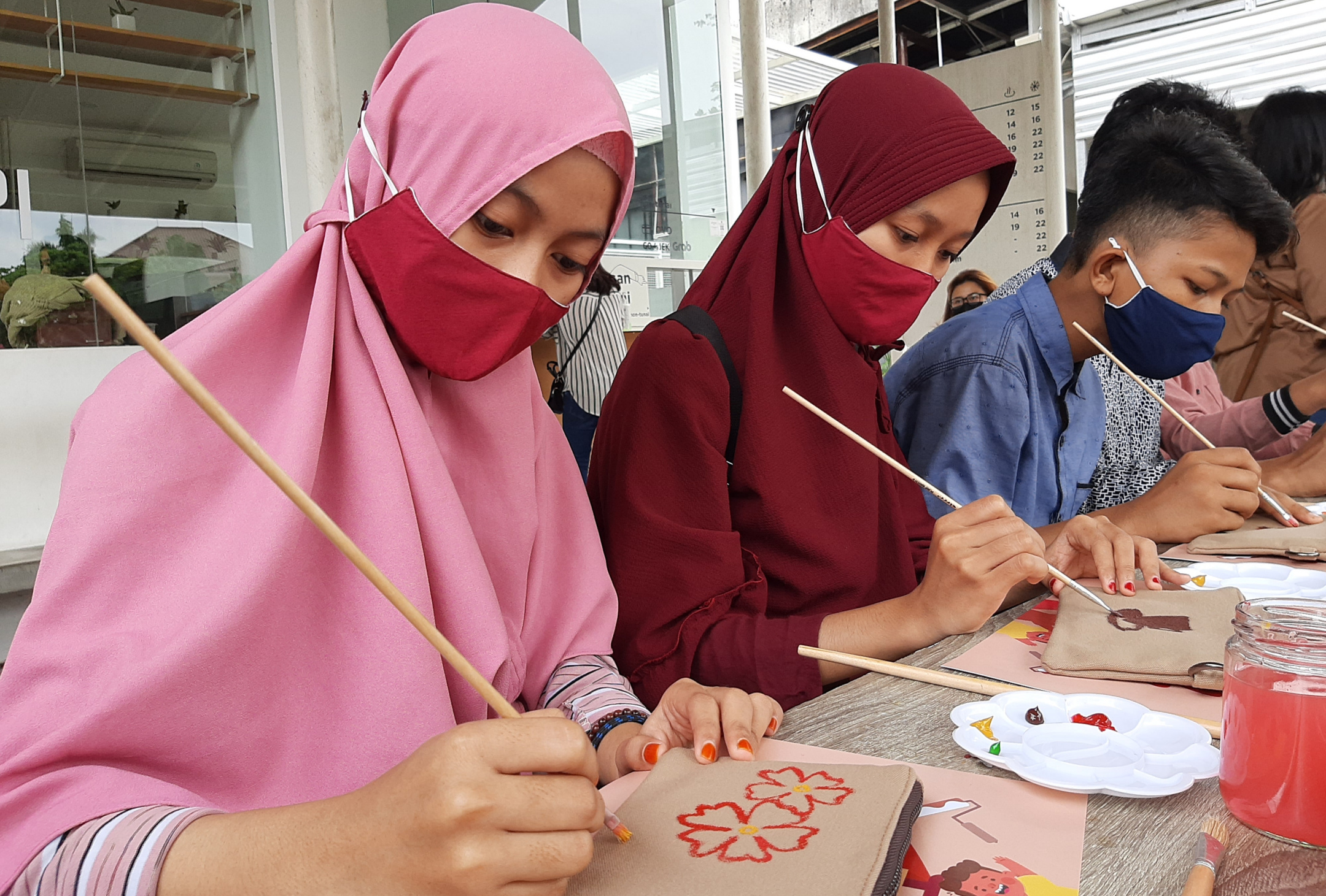 Ahmad Lucky dan teman-temannya sedang melukis diatas pouch kanvas water resist. (Foto: Pita Sari/Ngopibareng.id)