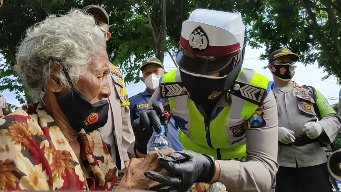 Seorang anggota Polresta Banyuwangi memberikan vitamin setelah memasangkan masker pada seorang nenek di kawasan Taman Blambangan, Banyuwangi, Jawa Timur. (Foto: Istimewa)