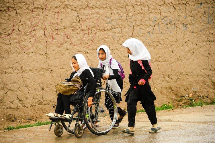 Dua gadis Afghanistan sedang membantu seorang ibu untuk berjalan di atas kursi roda. (Foto: afp)