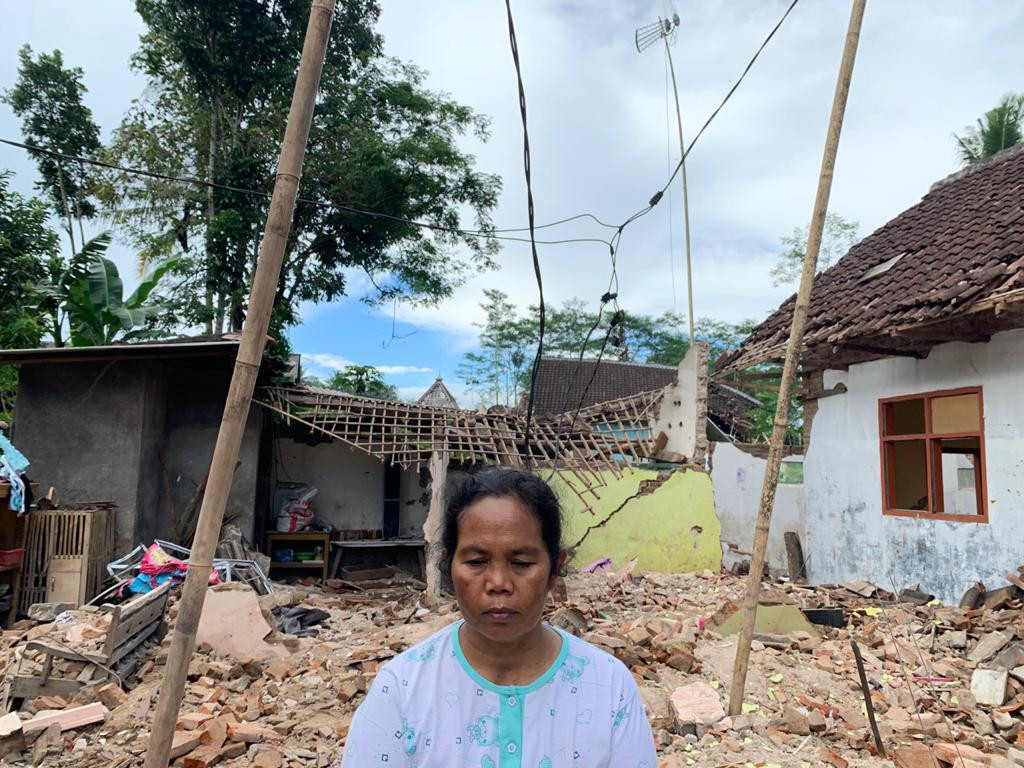 Warga Dampit, Kabupaten Malang, Mujiati dengan latar rumahnya yang hancur terdampak gempa bumi (Foto: Lalu Theo/ngopibareng.id)
