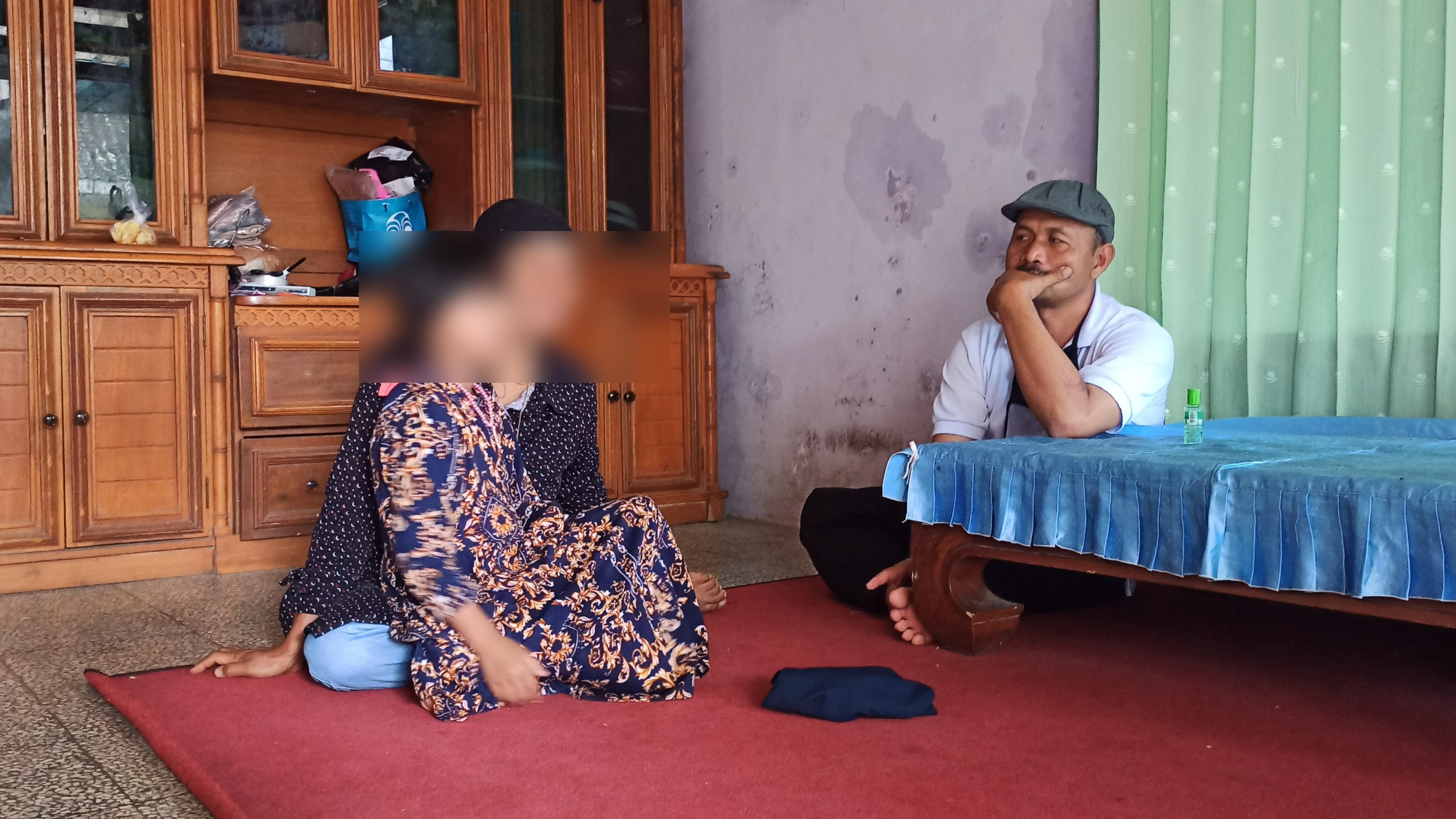 Tr duduk dipangkuan ibunya UH ditemani salah seorang perangkat Desa. Tr ditinggalkan ayah kandungnya US ratusan kileter dari rumahnya (foto Muh Hujaini/Ngopibareng.id)