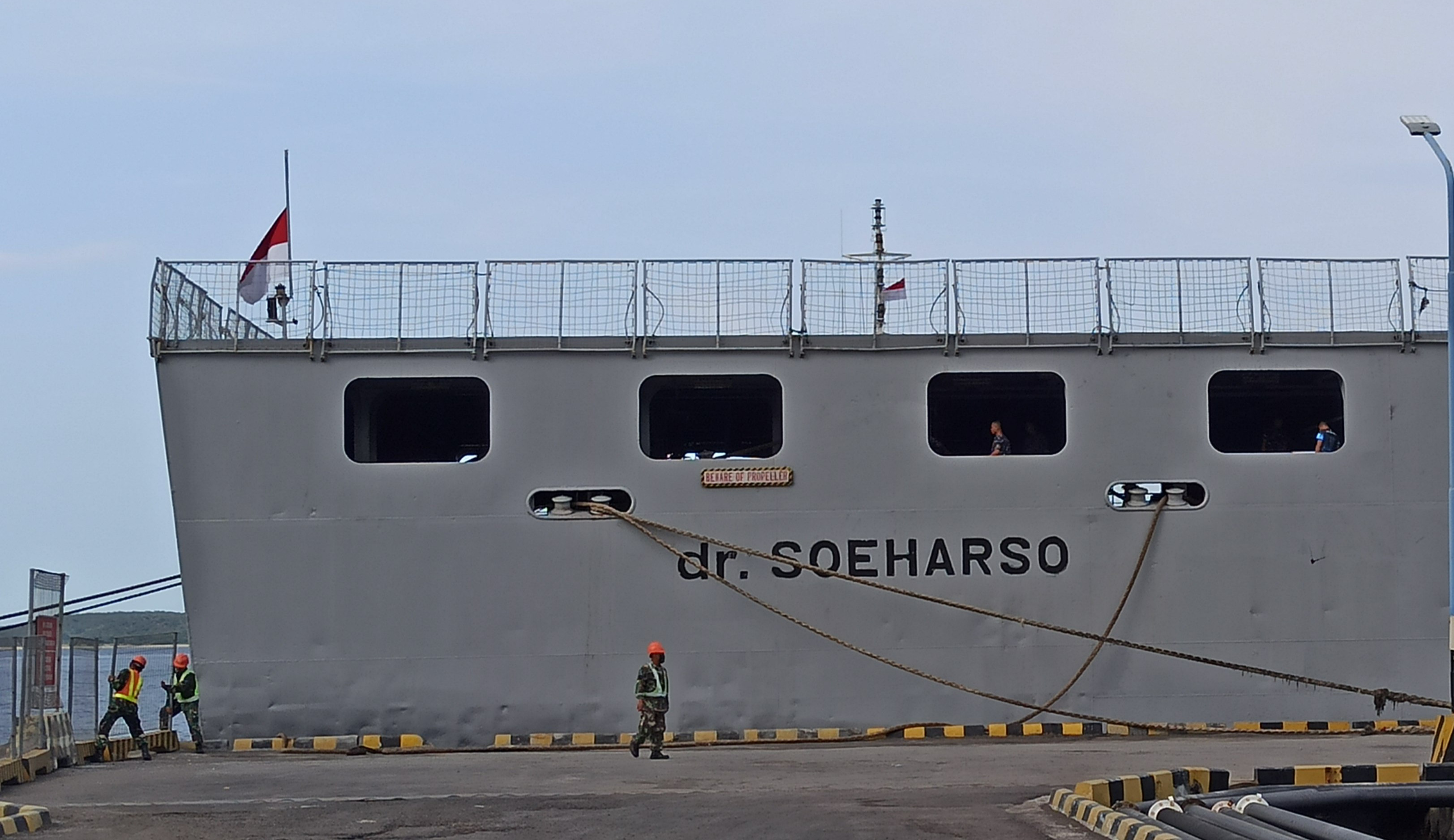 Sejumlah prajurit TNI AL sedang menambatkan tali dari KRI dr. Soeharso yang berlabuh di Pelabuhan Tanjungwangi Banyuwangi. Pada bagian geladak terlihat bendera merah putih yang dikibarkan setengah tiang (foto:Muh Hujaini/Ngopibareng.id)