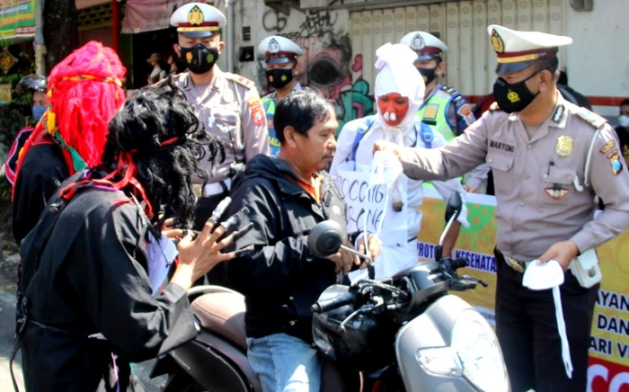 Anggota Satlantas Polres Bondowoso didampingi pocong dan jin hitam membagikan masker kepada pengendara sepeda motor. (Foto: Guido Saphan/Ngopibareng.id)