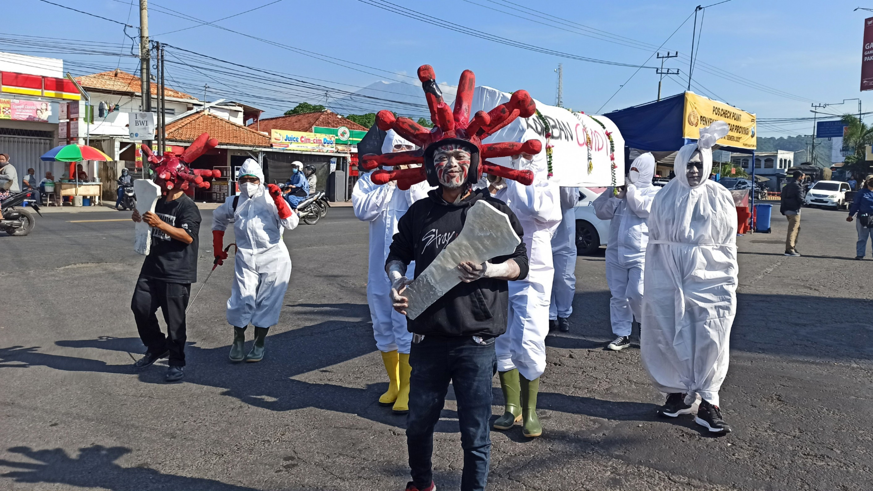 Aksi teatrikal dua orang yang berpakaian ala bentuk mikroskopik virus Covid-19 dan sejumlah orang berpakaian hasmat yang membawa keranda berisi korban Covid-19. (Foto: Muh Hujaini/Ngopibareng.id)