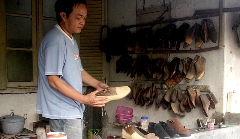 Ishak pemilik usaha Sepatoe Tjinta Bondowoso menunjukkan sepatu kulit pesanan pembeli dengan latar belakang cetakan sepatu di rumahnya. (Foto: Guido Saphan/Ngopibareng.id)