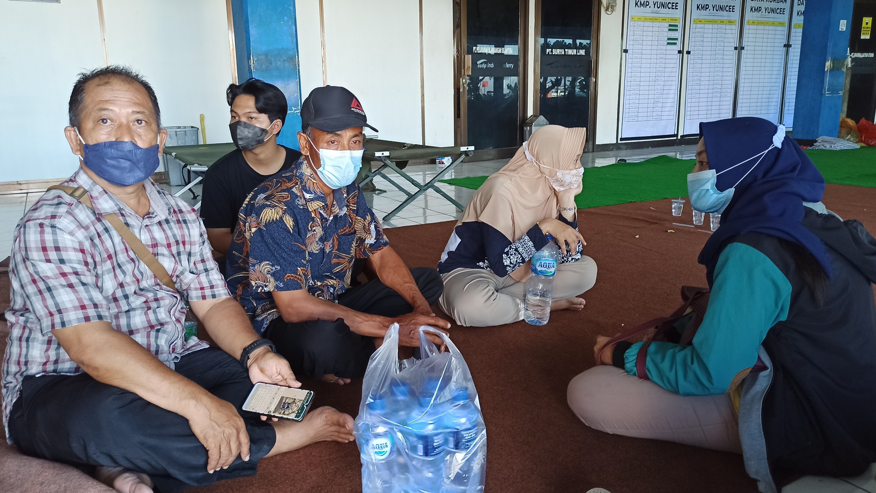 Minahadi (memakai batik) bersama keluarganya menunggu kabar adik dan dua keponakannya yang masih belum ditemukan di pelabuhan Ketapang (foto:Muh Hujaini/Ngopibareng.id)