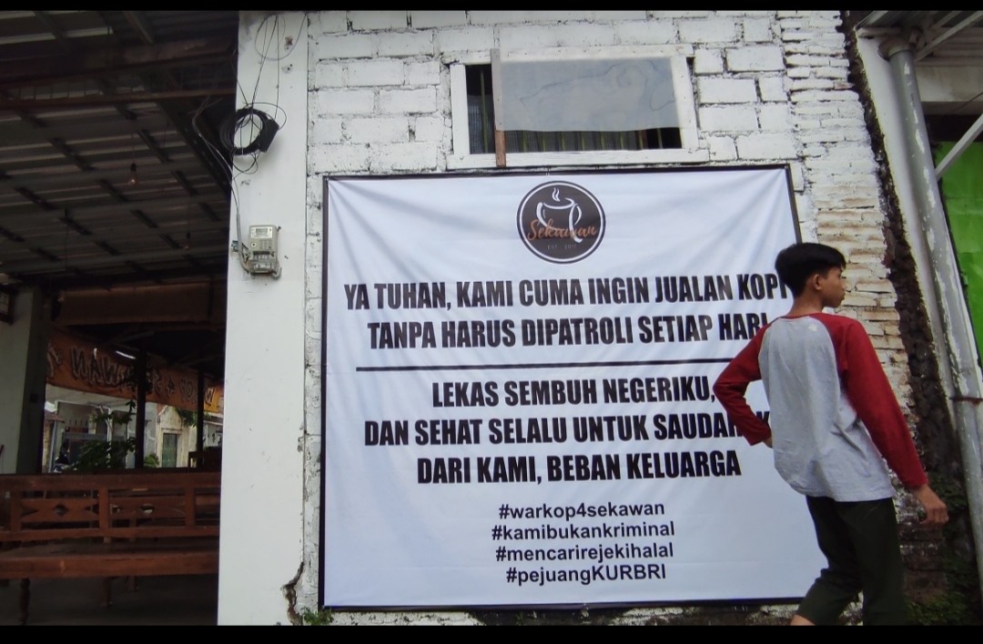 Warung kopi di Jalan Raya Kelurahan Bandar Kidul memasang spanduk berisi keluhan selama PPKM Darurat. (Foto: Fendhy Plesmana/Ngopibareng.id)