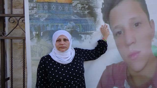 Bara'a Tamimi berdiri di samping poster putranya, Muhammad, yang ditembak dan dibunuh oleh tentara  Israel (Foto:Al Jazeera)