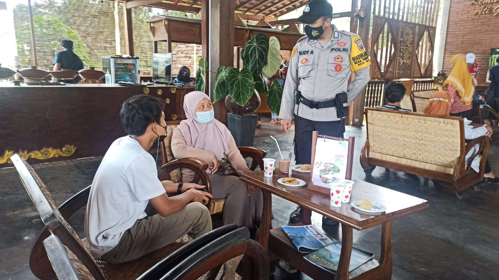 Salah satu polisi sedang berbincang dengan peserta vaksinasi yang menunggu giliran sambil menikmati kopi dankue gratis (Foto: Muh Hujaini/Ngopibareng.id)