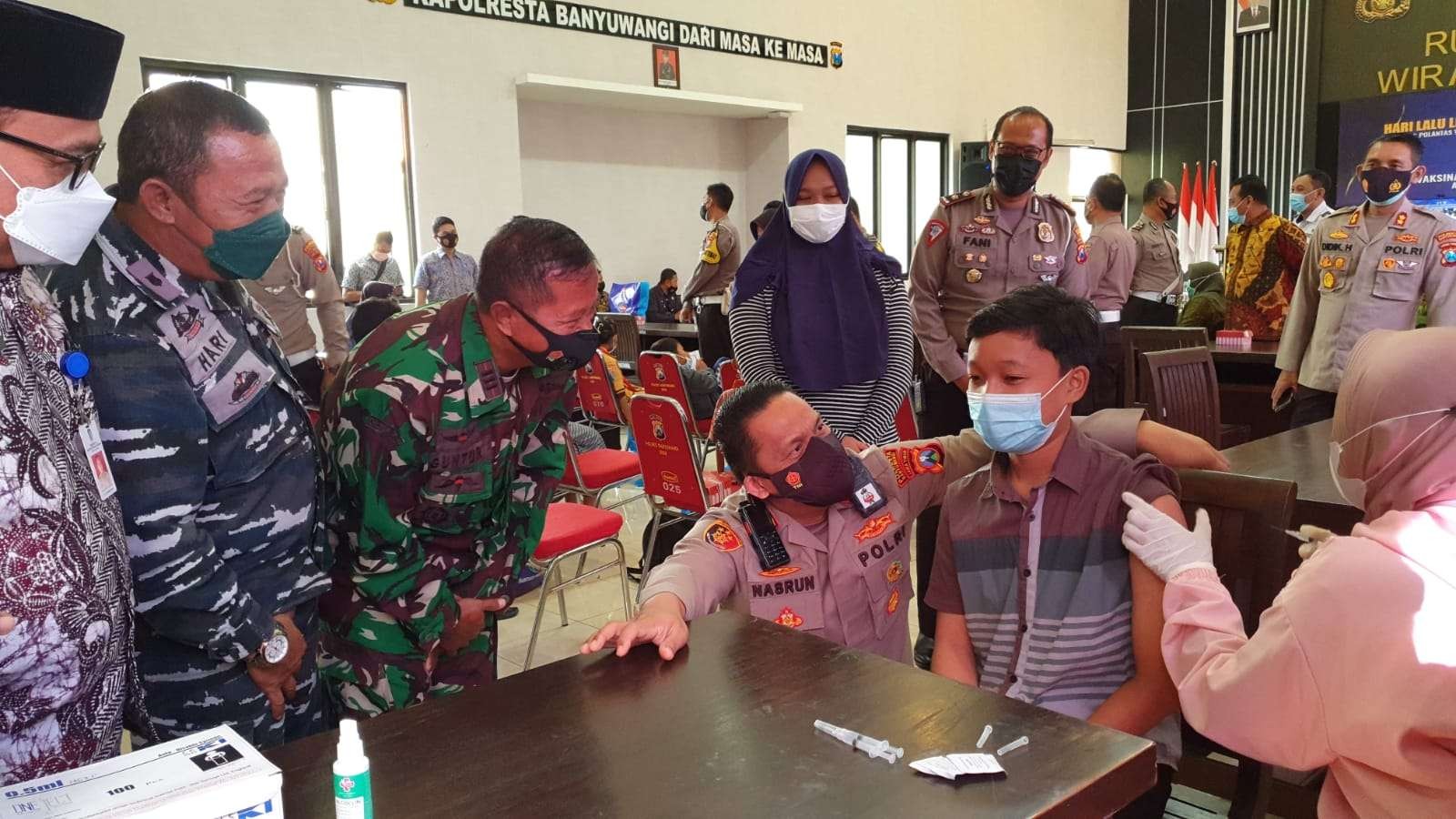 Kapolresta Banyuwangi AKBP Nasrun Pasaribu mendampingi salah seorang anak yatim menjalani vaksinasi Covid-19. (Foto: Istimewa)