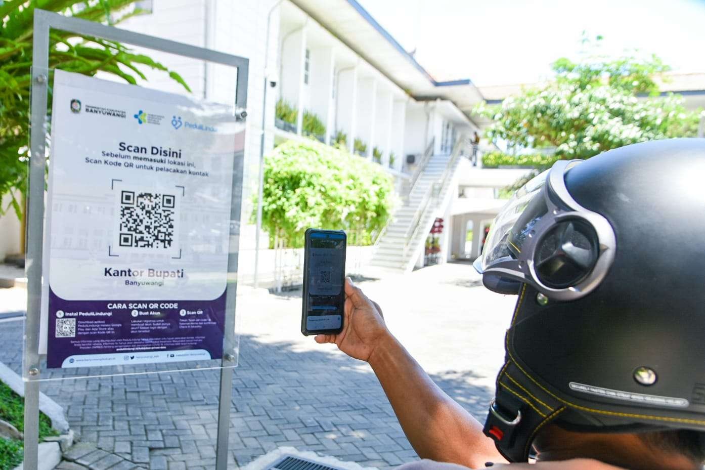 Salah seorang pengunjung Kantor Pemkab Banyuwangi men-scan QR Code dengan aplikasi PeduliLindungi (foto:istimewa)